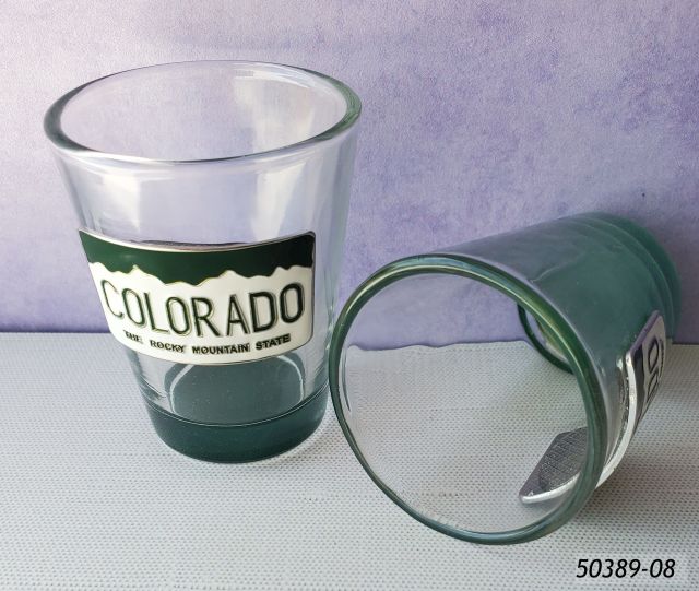 50389-08 Colorado Souvenir Glass shot with metal badge with Colorado license plate design glued to one side.  Green colored base. 