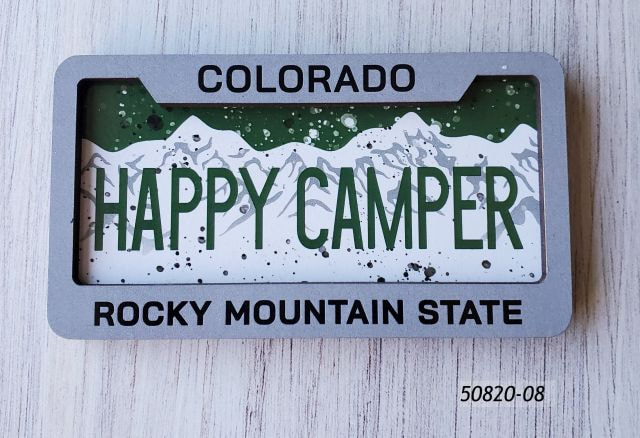 50820-08 Colorado Rectangular fiberboard magnet with two layers. Looks like a license plate inside a frame. Frame says Colorado Rocky Mountain State.  Inside graphic says Happy Camper and looks like the Colorado license plate but with a speckle overlay to imply campfire ware. 